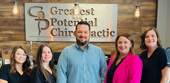 Dr. Marcus Woodburn with his staff in front of Greatest Potential Chiropractic sign.